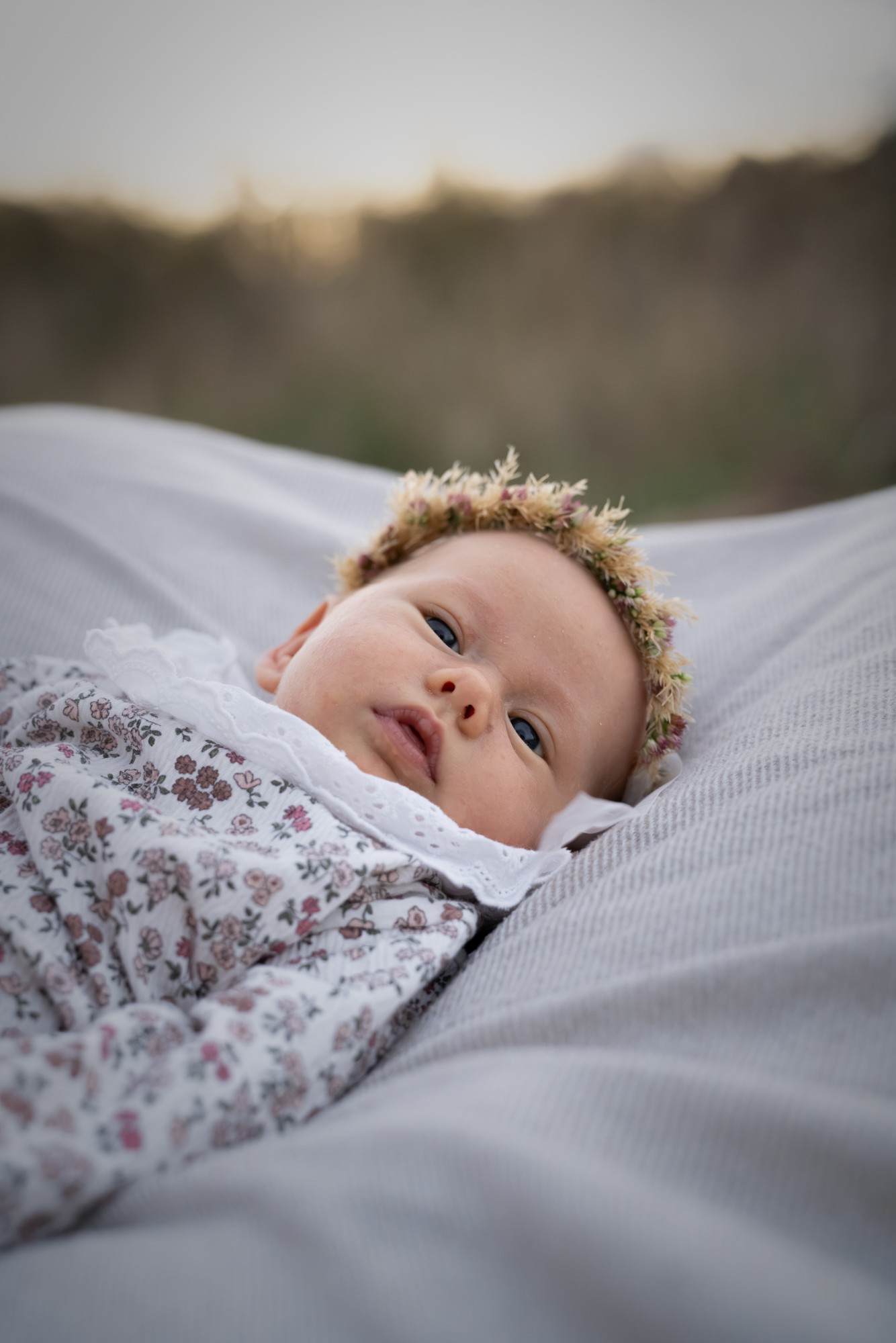Baby mit Blumenkranz auf einer hellen Decke, Blick zur Kamera