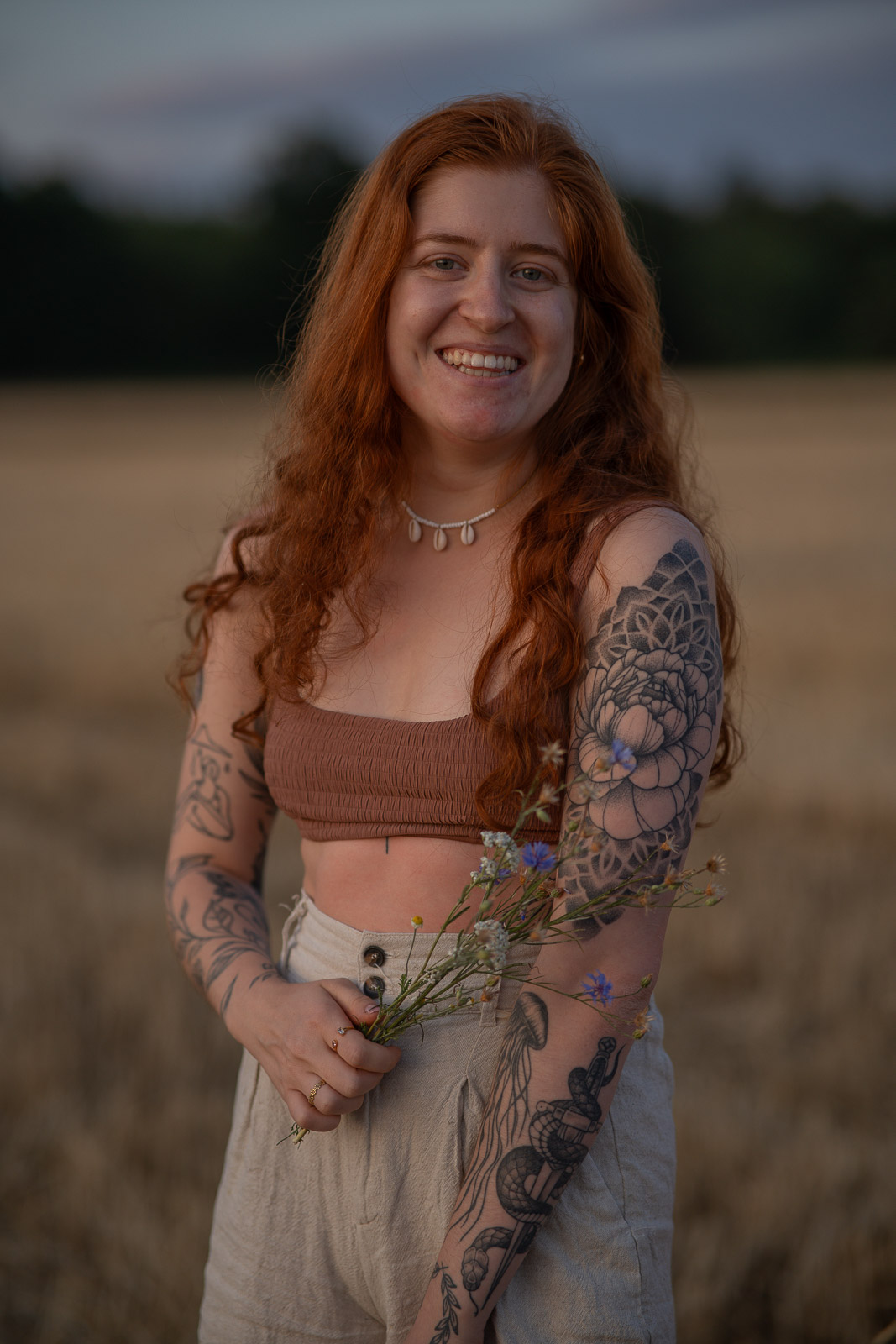 Porträt einer lachenden Frau mit Wildblumen im Feld bei Abendlicht